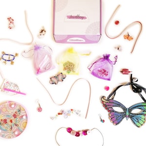 Peut inclure: Un assortiment de fournitures pour la fabrication de bijoux, comprenant des perles, des breloques et un masque de papillon. Les fournitures sont disposées sur un fond blanc avec une boîte rose portant l'inscription "Jewellery".