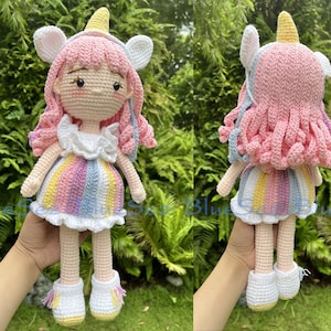 May include: A crocheted unicorn doll with pink hair, a rainbow striped dress, and white shoes. The doll is holding a white unicorn horn.