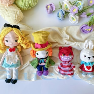 May include: A set of five crocheted amigurumi dolls, including Alice in Wonderland, the Mad Hatter, the Cheshire Cat, the White Rabbit, and a purple flower. The dolls are all handmade and have detailed features.