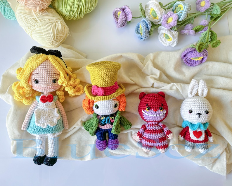 May include: A set of five crocheted amigurumi dolls, including Alice in Wonderland, the Mad Hatter, the Cheshire Cat, the White Rabbit, and a purple flower. The dolls are all handmade and have detailed features.