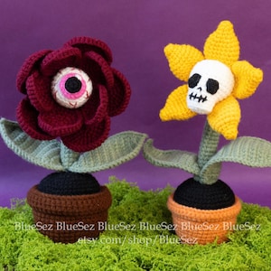 May include: Two crocheted flower pots, one with a red flower with an eye and the other with a yellow flower with a skull face.
