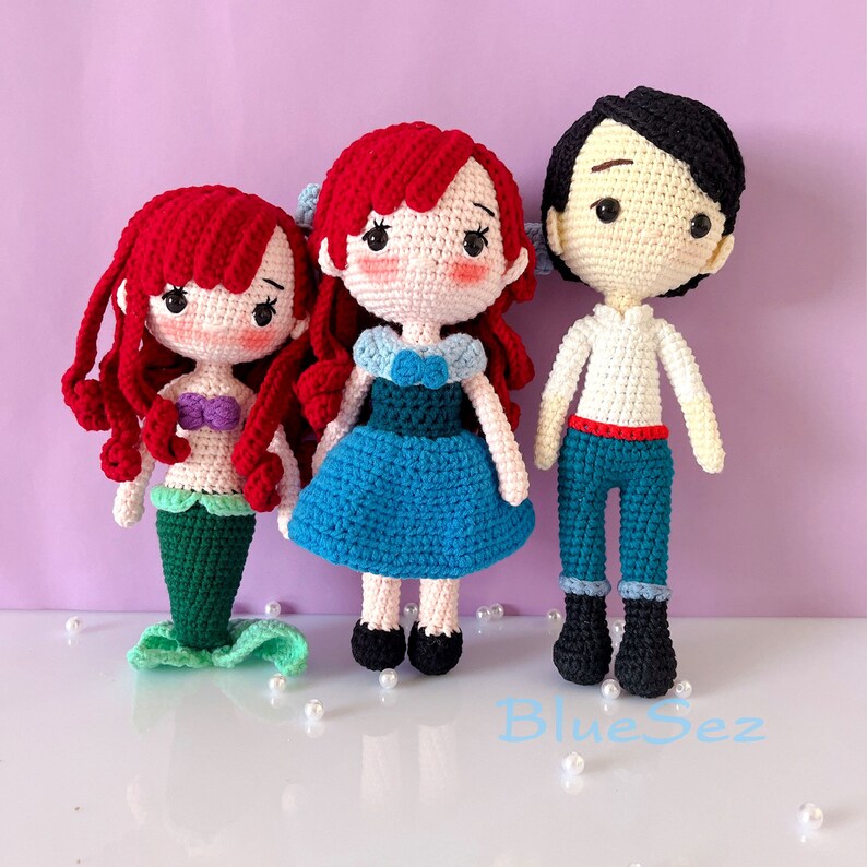 May include: Three handmade crochet dolls. One is a mermaid with a green tail and purple top, the other is a princess in a blue dress, and the last is a prince in a white shirt and blue pants. All dolls have black eyes and red or black hair.