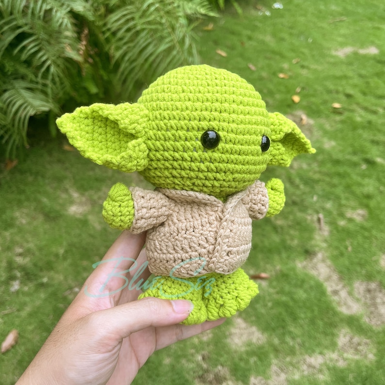 K&ouml;nnte beinhalten: Ein geh&auml;keltes Pl&uuml;schtier in Gr&uuml;n und Braun, das einem Charakter aus dem Star Wars-Franchise &auml;hnelt. Das Spielzeug hat gro&szlig;e Ohren, einen kleinen Mund und schwarze Augen.