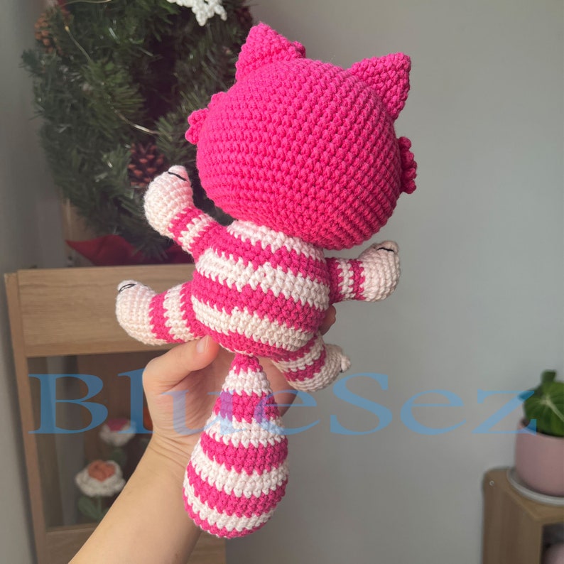 May include: Pink and white striped crocheted cat toy. The cat has a long tail and is sitting up with its paws outstretched.