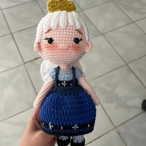 May include: A crocheted doll with white hair, a gold crown, a blue dress with a white bib, and black shoes.