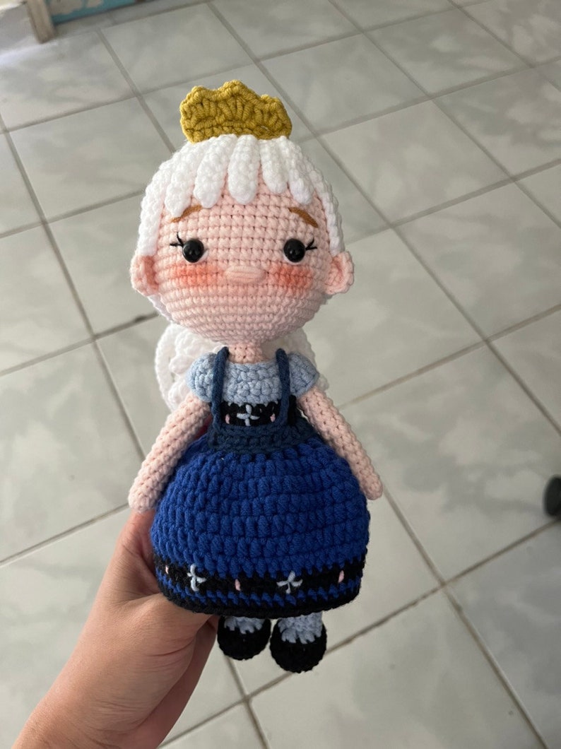 May include: A crocheted doll with white hair, a gold crown, a blue dress with a white bib, and black shoes.
