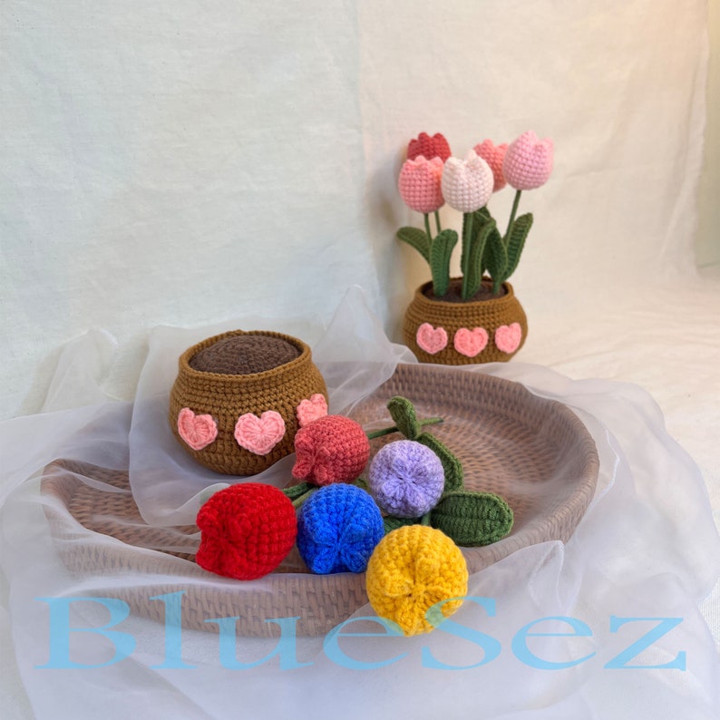 May include: A set of five crocheted tulips in red, yellow, blue, purple, and pink. The tulips are arranged in a brown wicker basket. The tulips are all in bloom and have green leaves.