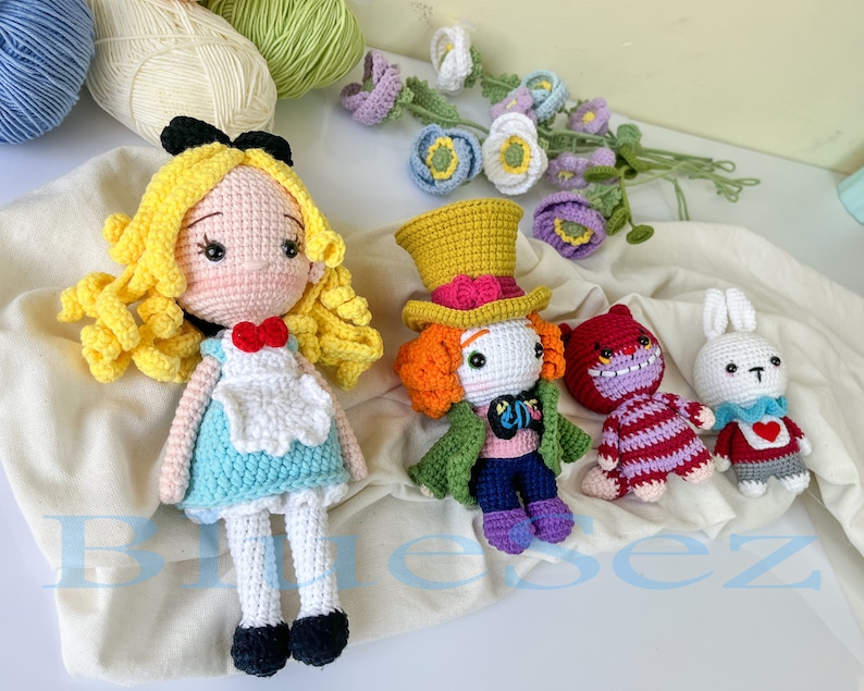 May include: Crocheted Alice in Wonderland characters, including Alice, the Mad Hatter, the Cheshire Cat, and the White Rabbit. The characters are all wearing colorful clothing and have detailed facial features.