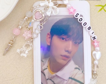May include: A white photo card holder with a photo of a person, attached to a silver keychain. The holder is decorated with pink and white beads, a bow, and charms. The name "SOOBIN" is spelled out in white letter beads.