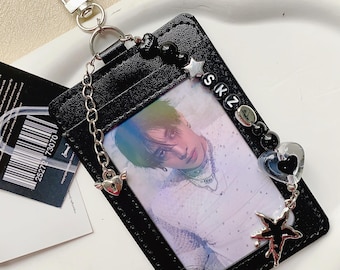 May include: Black leather ID holder with a photo of a person. The holder has a silver chain and a lobster clasp. Decorative beads, a star, and a heart charm are attached. The letters "SKZ" are on the holder.