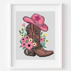 May include: A framed print featuring a brown cowboy boot with floral accents and a pink cowboy hat. The boot is adorned with decorative patterns and a rope detail. Pink and yellow flowers surround the boot and hat, creating a country-themed design.