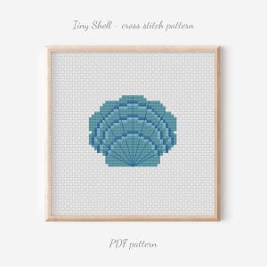 May include: A framed cross-stitch pattern featuring a blue seashell design. The artwork is set against a white background and framed in a light wood. Text at the top reads "Tiny Shell - cross stitch pattern" and at the bottom "PDF pattern".