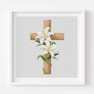 May include: Cross-stitch art of a wooden cross adorned with white lilies and green leaves. The cross is a light brown color, and the lilies have yellow centers. The artwork is framed in a white square frame.
