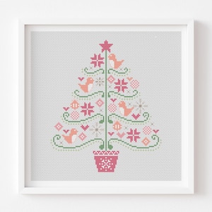 May include: A framed cross-stitch Christmas tree design. The tree features pink and green decorations, birds, and snowflakes. A pink star sits atop the tree, which is planted in a pink pot. The background is light grey.