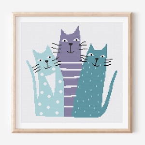Op de afbeelding: Een ingelijste print met drie gestileerde katten in blauwe en paarse tinten. De katten hebben zwarte snorharen en zijn versierd met stippen en strepen. Het kunstwerk staat tegen een witte achtergrond.