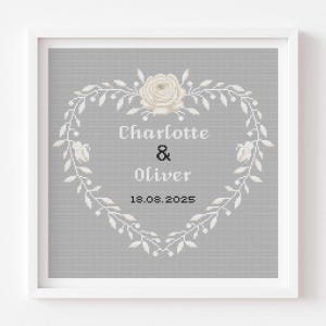 Könnte beinhalten: Gerahmtes Kreuzstich-Kunstwerk mit einem herzförmigen Kranz und einer cremefarbenen Rose. Die Namen "Charlotte & Oliver" und das Datum "18.08.2025" sind auf grauem Hintergrund innerhalb des Kranzes zu sehen. Der Rahmen ist weiß.