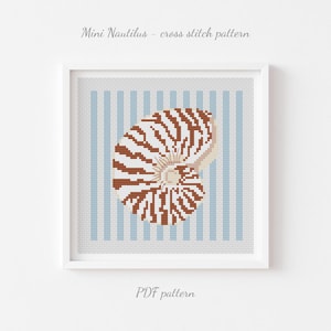 May include: A framed cross-stitch pattern featuring a nautilus shell in shades of brown and white, set against a light blue and white striped background. The text "Mini Nautilus - cross stitch pattern" and "PDF pattern" are displayed.
