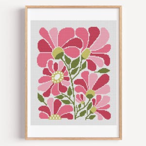 May include: Framed floral cross-stitch art featuring stylized pink flowers with green leaves and yellow centers. The flowers are arranged in a symmetrical pattern against a light gray background, encased in a wooden frame.