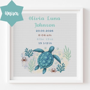 May include: A framed cross-stitch art piece featuring a teal sea turtle, seaweed, and crabs. The artwork includes the name "Olivia Luna Johnson", birthdate, time, weight (6lbs 15oz), and length (19 1/2in). A teal "unisex" tag is in the upper left corner.