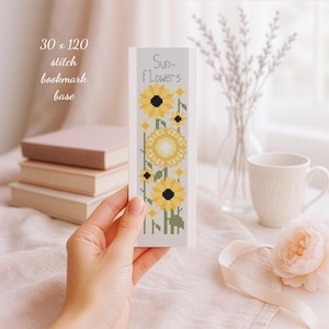 Könnte beinhalten: Ein handgefertigter Lesezeichen mit einem Sonnenblumenmuster. Das Lesezeichen zeigt gelbe und schwarze Sonnenblumen mit grünen Stielen und Blättern. Der Text "Sun-flowers" ist oben aufgedruckt. Das Lesezeichen wird in einer Hand gehalten, mit Büchern und einer Tasse im Hintergrund.