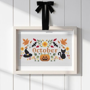 Pode incluir: Um bordado em ponto cruz emoldurado com a palavra October em letras laranja, rodeada por uma abóbora, um gato preto, um chapéu de bruxa, morcegos e folhas de outono em tons de laranja, amarelo, vermelho e verde, com um laço preto no topo.
