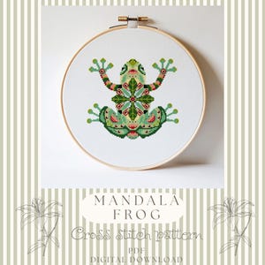 May include: A cross stitch pattern featuring a stylized frog with a symmetrical mandala design in shades of green, red, and cream, displayed in a round wooden embroidery hoop. The text reads MANDALA FROG Cross Stitch pattern PDF DIGITAL DOWNLOAD.