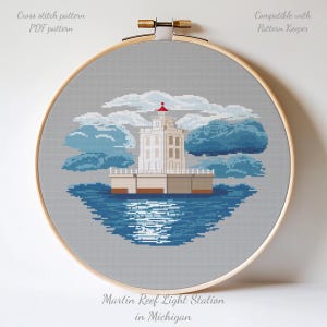 May include: A cross-stitch pattern of the Martin Reef Light Station in Michigan, presented in a wooden embroidery hoop. The design shows a white lighthouse with a red top, set against blue clouds and water. Text includes "Cross stitch pattern PDF pattern" and "Compatible with Pattern Keeper".