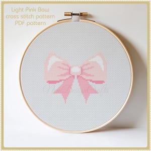 May include: A light pink bow cross stitch pattern in a white embroidery hoop. The pattern is for a PDF download.