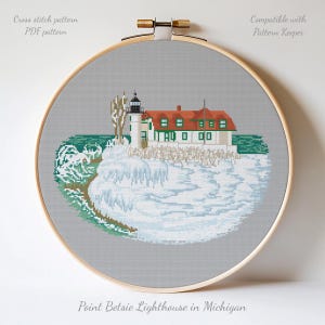 May include: A cross-stitch pattern of Point Betsie Lighthouse in Michigan, displayed in a wooden embroidery hoop. The design features the lighthouse with a red roof, white walls, and green window frames, set against a gray background. The text "Cross stitch pattern PDF pattern" is visible.