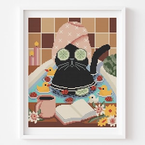 Puede incluir: Una obra de arte de punto de cruz enmarcada representa a un gato negro relajándose en un baño con rodajas de pepino en los ojos. El gato está rodeado de patitos de goma, mariquitas y flores. Una taza rosa y un libro abierto están en el estante.