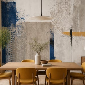 Op de afbeelding: Een eetkamer met een rechthoekige houten tafel omringd door zes mosterdgele gestoffeerde stoelen. De muur achter de tafel toont een grote muurschildering met abstracte blokken van donkerblauwe, grijze en gele verftexturen.
