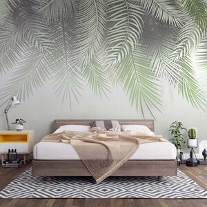 K&ouml;nnte beinhalten: Ein Schlafzimmer mit einem Bett, einem Nachttisch und einem Teppich. Die Wand ist mit einer gro&szlig;fl&auml;chigen Tapetenmusterung aus Palmbl&auml;ttern verziert. Das Bett hat eine wei&szlig;e Bettdecke und eine braune Tagesdecke. Der Nachttisch ist gelb und wei&szlig; und hat eine Lampe darauf. Der Teppich ist schwarz und wei&szlig; und hat ein geometrisches Muster.