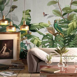 Puede incluir: Un sof&aacute; blanco con tres l&aacute;mparas colgantes doradas sobre &eacute;l. La pared detr&aacute;s del sof&aacute; est&aacute; cubierta con un papel tapiz tropical con hojas verdes, un loro y mariposas.