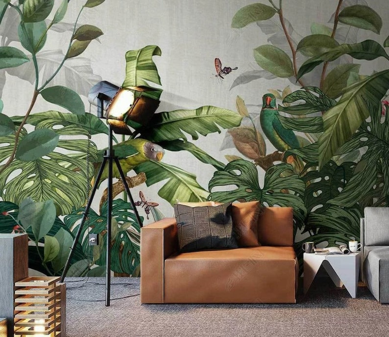 Puede incluir: Un sof&aacute; de cuero marr&oacute;n con dos almohadas se encuentra frente a un mural tropical con hojas verdes, un p&aacute;jaro y una mariposa. Una l&aacute;mpara de tr&iacute;pode negra con un foco est&aacute; en primer plano.