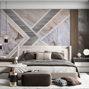 Puede incluir: Un dormitorio con una cama con estructura blanca y un papel tapiz con estampado geom&eacute;trico que presenta un dise&ntilde;o de m&aacute;rmol. La cama tiene un edred&oacute;n blanco y almohadas marrones. Hay dos mesitas de noche con l&aacute;mparas y una peque&ntilde;a mesa redonda con base dorada.