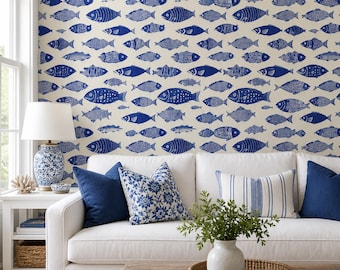 May include: A living room with a white sofa, blue pillows, and a wooden coffee table. The wall is covered in a blue fish pattern wallpaper. A white side table holds a lamp and decorative items. A woven rug covers the floor.