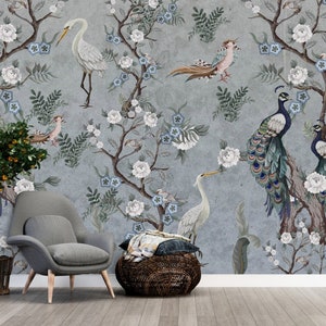 May include: A gray wall mural with a floral design featuring white flowers, blue flowers, and green leaves. There are peacocks, a heron, and other birds in the design. The mural is in a room with a gray armchair and a woven basket.
