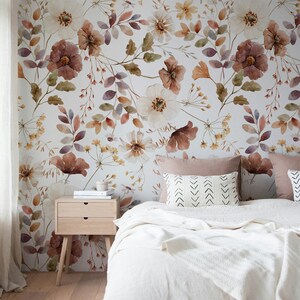Puede incluir: Un dormitorio con una cama blanca, una mesita de noche de madera y un papel tapiz floral. El papel tapiz presenta un dise&ntilde;o de acuarela de flores y hojas en tonos marrones, rosas y amarillos.