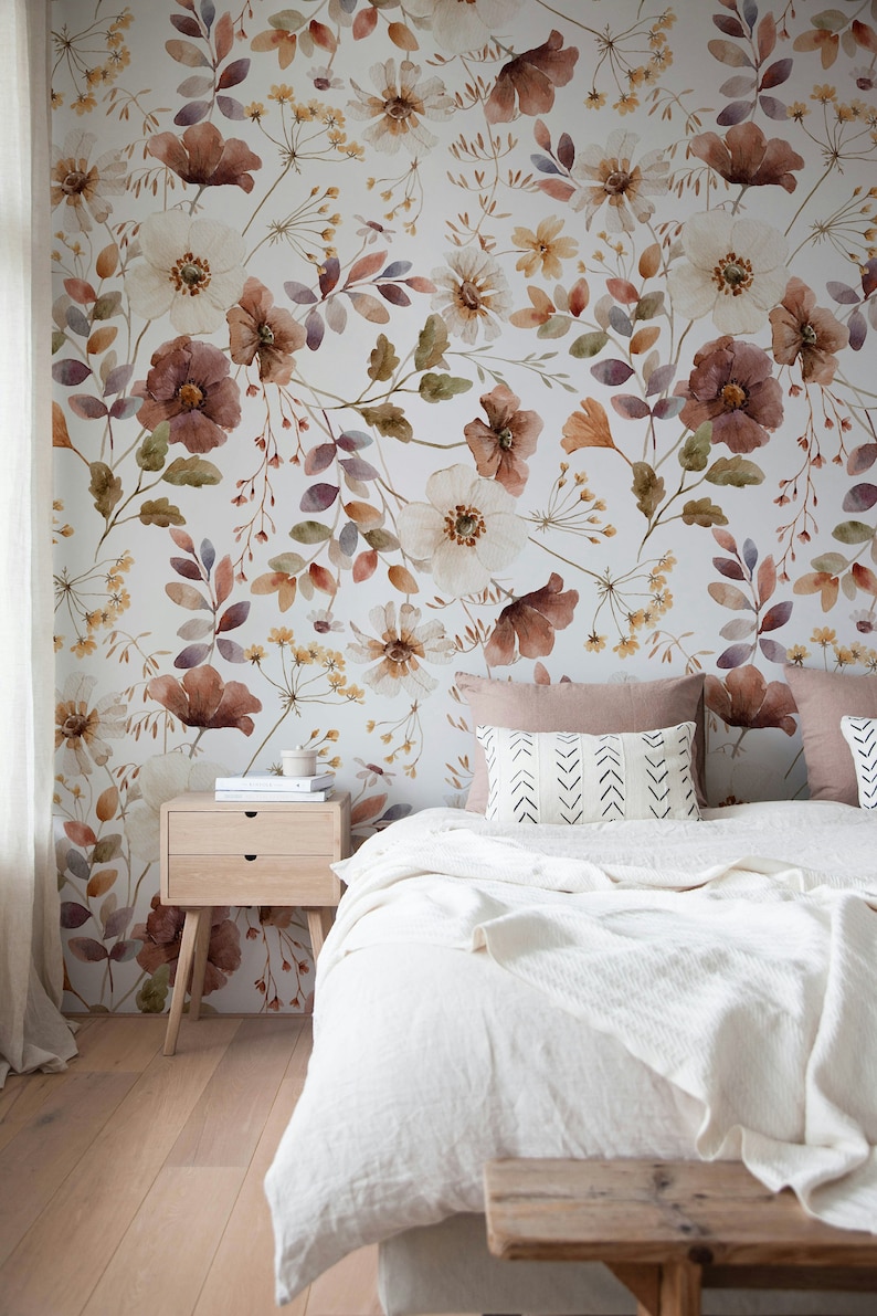 Puede incluir: Un dormitorio con una cama blanca, una mesita de noche de madera y un papel tapiz floral. El papel tapiz presenta un dise&ntilde;o de acuarela de flores y hojas en tonos marrones, rosas y amarillos.