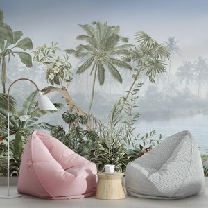 May include: Two bean bag chairs, one pink and one gray, are placed in front of a tropical mural. The mural depicts a lush jungle scene with palm trees, a lake, and lily pads. A small wooden table with a white cup sits between the chairs.