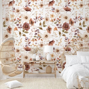 Puede incluir: Un interior de dormitorio con un papel tapiz floral blanco con flores marrones y blancas. Una silla colgante de mimbre y una cama con ropa de cama blanca est&aacute;n en la habitaci&oacute;n. Una mesa de madera con una l&aacute;mpara y libros est&aacute; en primer plano.
