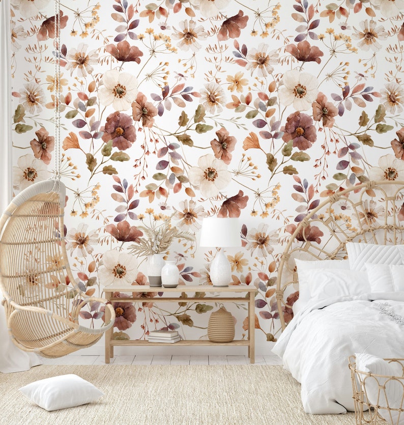 Puede incluir: Un interior de dormitorio con un papel tapiz floral blanco con flores marrones y blancas. Una silla colgante de mimbre y una cama con ropa de cama blanca est&aacute;n en la habitaci&oacute;n. Una mesa de madera con una l&aacute;mpara y libros est&aacute; en primer plano.