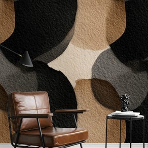 May include: An interior design scene featuring a brown leather armchair with black metal frame, a small side table, and a black lamp. The background is a textured wall with overlapping abstract shapes in black, brown, and beige.
