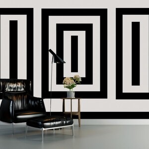 Puede incluir: Un sill&oacute;n de cuero negro con un reposapi&eacute;s a juego se encuentra frente a una pared blanca con un patr&oacute;n geom&eacute;trico en blanco y negro. Una peque&ntilde;a mesa auxiliar de madera con una planta en maceta se encuentra junto al sill&oacute;n.