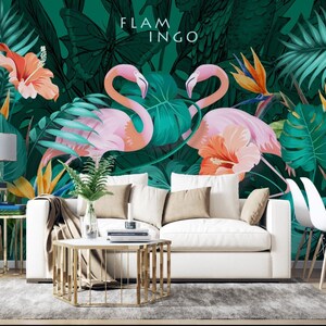 May include: A white couch with pillows sits in front of a tropical mural featuring pink flamingos, green leaves, and orange flowers. The text "FLAMINGO" is written in black letters on the mural.