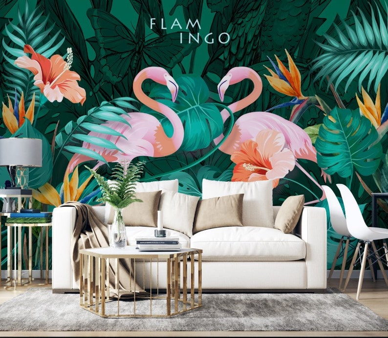 May include: A white couch with pillows sits in front of a tropical mural featuring pink flamingos, green leaves, and orange flowers. The text "FLAMINGO" is written in black letters on the mural.