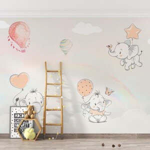May include: A nursery wall mural with a pastel pink, gray, and white color scheme. The mural features a rainbow, clouds, butterflies, and elephants holding balloons. The text "ABCDE GH I J K L M N O P Q R S T U V W X Y Z" is printed on a framed canvas.