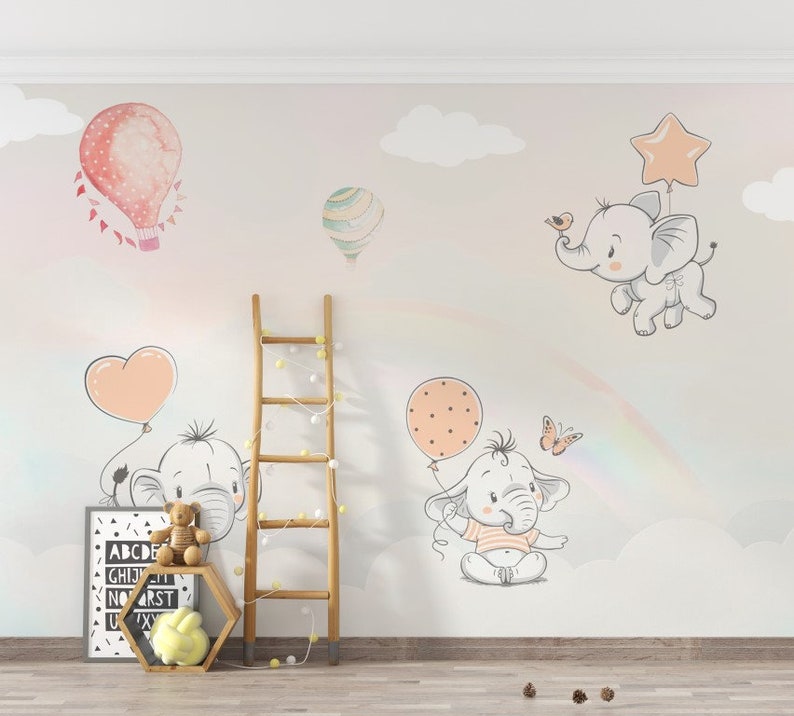 May include: A nursery wall mural with a pastel pink, gray, and white color scheme. The mural features a rainbow, clouds, butterflies, and elephants holding balloons. The text "ABCDE GH I J K L M N O P Q R S T U V W X Y Z" is printed on a framed canvas.