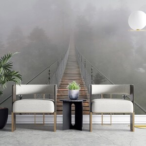 May include: Two white chairs with gold legs sit in front of a foggy forest scene with a suspension bridge leading into the distance. A floor lamp with a white globe sits to the right of the chairs.