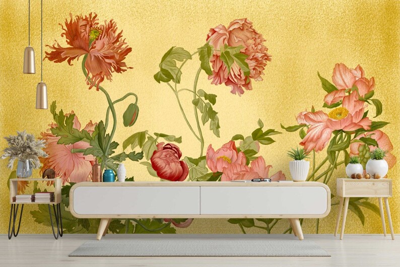 May include: A floral wallpaper mural with a gold background featuring pink and red flowers with green leaves. The wallpaper is displayed in a living room setting with a white console table and two side tables.